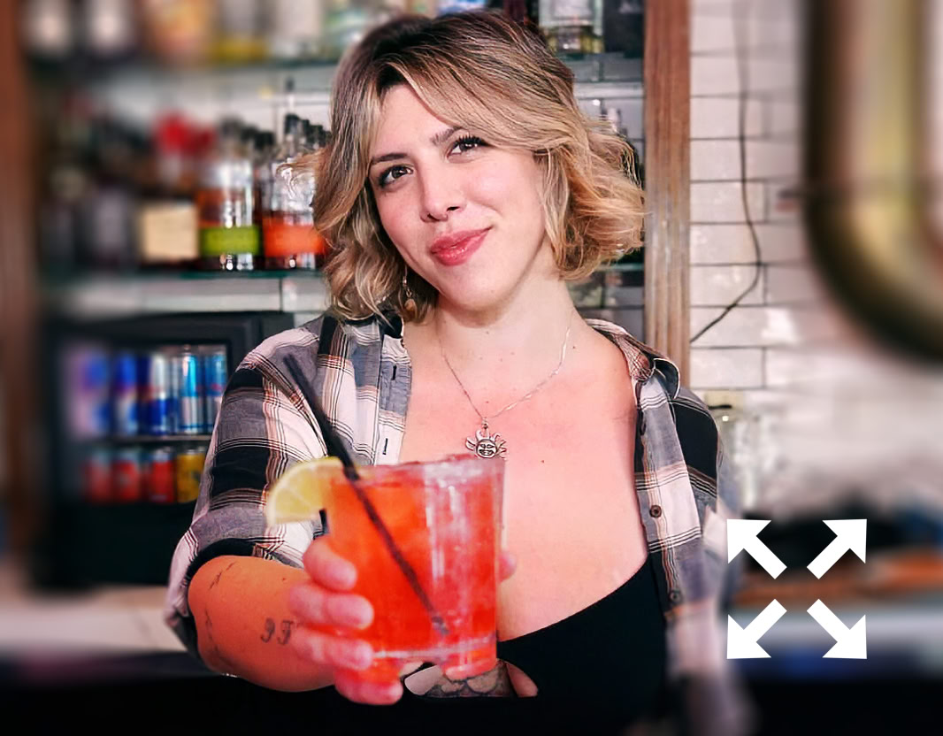 A bartender carefully adds a garnish to a cocktail using tweezers at a bar counter.